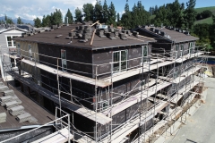 aerial view of dwelling units under construction and surrounded by scaffolding with roof finish material stacked on the rooftops