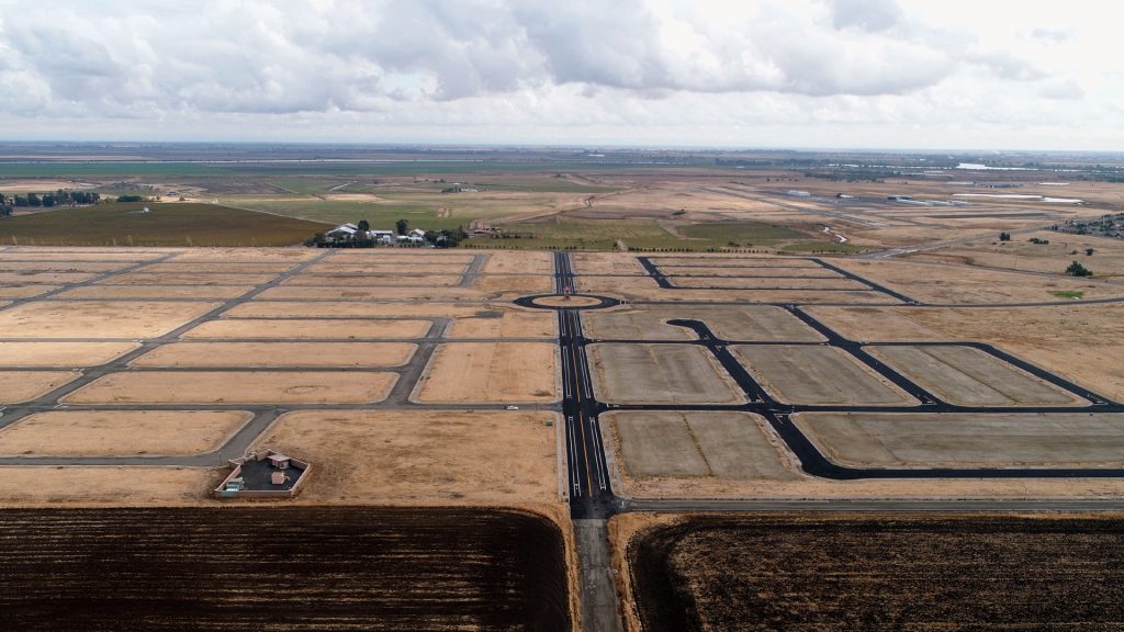 land at beginning stages of development with paved streets and empty lots, and open land in the background
